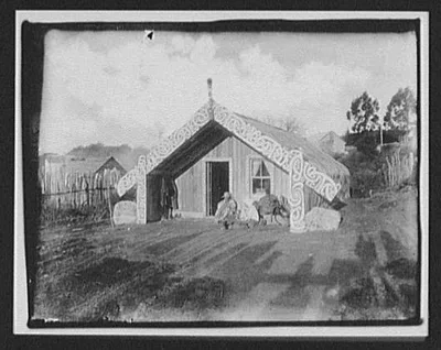 Man, woman and baby in front of ornamented Maori house, New Zealand, 1895